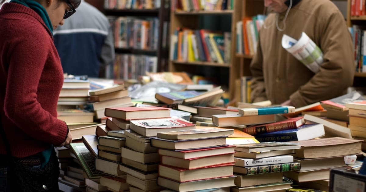 homem e mulher ao lado de uma pilha de livros a venda